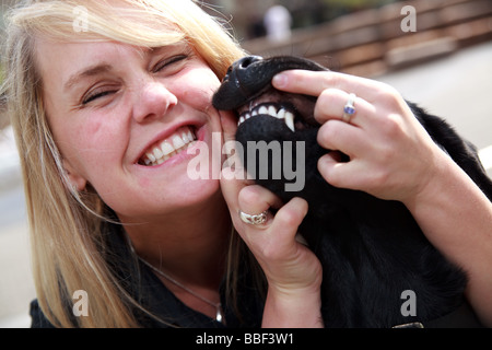 Blondine mit weißen kaukasischen Frau mit schwarzen Labrador Guide Hund in eine urbane Parklandschaft. Stockfoto