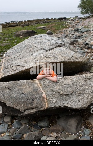 Ein kleiner Junge spielt in einem massiven geknackt Felsbrocken entlang des Ufers in Connecticut USA Stockfoto