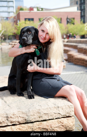 Blondine mit weißen kaukasischen Frau mit schwarzen Labrador Guide Hund in eine urbane Parklandschaft. Stockfoto