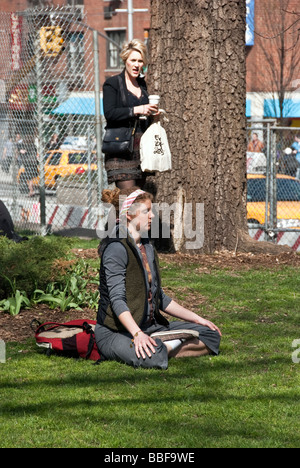 eine junge rote behaarte Frau mit rosigen Wangen & Sommersprossen sitzt mit gekreuzten Beinen meditieren im Union Square Park in New York City Stockfoto