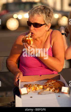 mittlere gealterte Frau Essen ein Stück Pizza aus einem Take-away-Karton im freien Sommerabend, UK Stockfoto