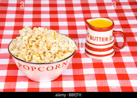 Eine Schüssel mit heißen frisch fertiges Popcorn und eine Tasse geschmolzene Butter auf einer rot-weiß karierte Tischdecke Stockfoto