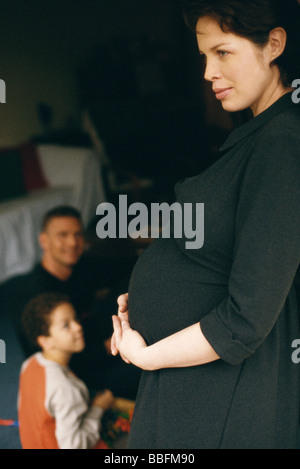 Schwangere Frau mit Bauch, Ehemann und Sohn im Hintergrund Stockfoto