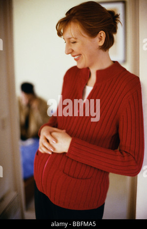 Schwangere Frau in Tür mit Händen stützte sich auf Magen, Lächeln Stockfoto