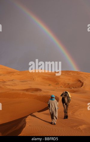 Afrika, Nordafrika, Marokko, Sahara Wüste, Merzouga, Erg Chebbi, Berber Tribesman führenden Kamel, Regenbogen in der Wüste Stockfoto