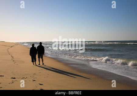 Paar bei Sonnenaufgang am Strand entlang schlendern.