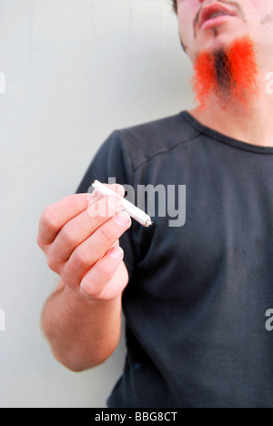 Junger Mann mit rot-schwarzen Bart hält eine gemeinsame, handgerollte Zigarette rauchen Unkraut Stockfoto