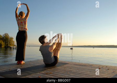 Frau und Mann beim Yoga auf einem hölzernen Pier an einem See Stockfoto