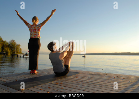 Frau und Mann beim Yoga auf einem hölzernen Pier an einem See Stockfoto
