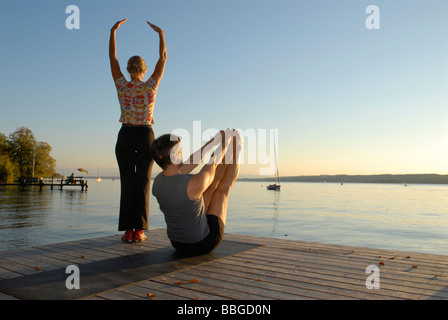 Frau und Mann beim Yoga auf einem hölzernen Pier an einem See Stockfoto