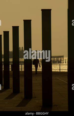 Silhouette am Meer Blick eines Mannes zu Fuß vorbei an der "Stream"-Kunst-Instillation in St Leonards mit Hastings Pier hinter. Stockfoto