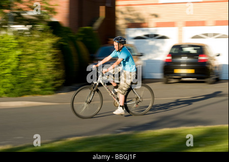 Junge Teenager, die mit dem Fahrrad mit Geschwindigkeit entlang einem Vorort Straße im Sommer in England Stockfoto