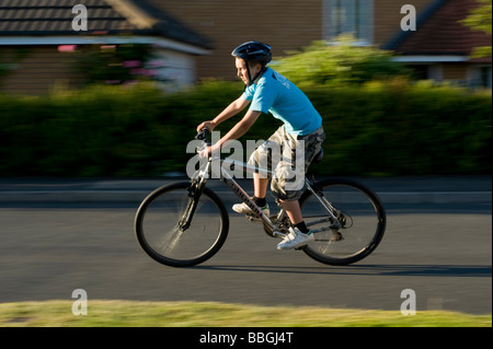 Junge Teenager, die mit dem Fahrrad mit Geschwindigkeit entlang einem Vorort Straße im Sommer in England Stockfoto