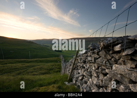 Bei Sonnenuntergang führt eine Trockenmauer das Auge entlang Littondale, in den Yorkshire Dales, von oben das Dorf Arncliffe. Stockfoto