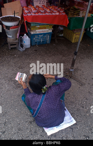 Alte Frau sitzt auf dem Boden auf einem Markt in Chiang Mai Thailand Lottoscheine verkauft Stockfoto