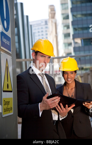 Zwei Führungskräfte von ein Mann und eine Frau tragen Schutzhelme prüfen Pläne in einer modernen Stadt Stockfoto