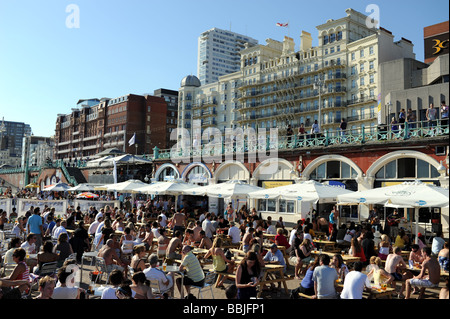 Menschenmassen am Strand von Brighton und an der Gemini-Bar an der Strandpromenade UK mit Grand Hotel im Hintergrund Stockfoto