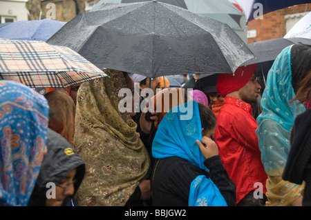 Sikhs halten Sonnenschirme, da es stark auf die Vaisakhi Prozession in Manor Park, London regnet. Stockfoto