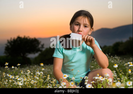 junges Mädchen mit einem Eis am Stiel in eine Blumenfeld bei Sonnenuntergang Stockfoto