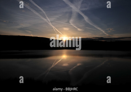 Roter Sonnenuntergang hinter den Hügeln am Rande des Sees Gewässer reflektierenden Flugzeuge Kondensstreifen, in der Nähe von Denshaw, größere Manchester, UK Stockfoto