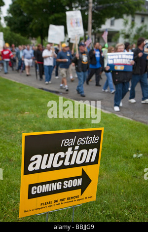 Gewerkschaftsmitglieder marschieren für Jobs passieren Schild kündigt die Versteigerung eines Hauses Stockfoto