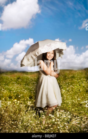 junges Mädchen im weißen Kleid mit Sonnenschirm in einem Blumenfeld Stockfoto