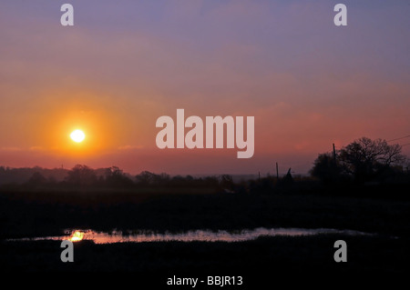 Roter Sonnenaufgang über dem Wasser in einem Feld in der Grafschaft Kent, in der Nähe von Great Chart, Ashford, Vereinigtes Königreich Stockfoto