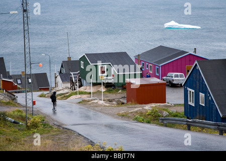 Man überquert die Straße, bunte Häuser und Eisberg.  Qaqortoq (Julianehåb), Süd-Grönland Stockfoto