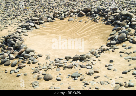 Felsen in einem Kreis angeordnet über Sand mit Wellen Stockfoto