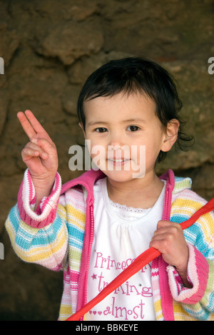 Ein halb-Thai-Mädchen sitzt am unteren Ende einer Wand an einem sonnigen Sommertag in Skegness macht ein Handzeichen Stockfoto