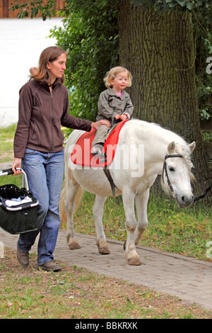 eine Mutter hält ihr kleines Mädchen, das ein Pony reiten ist Stockfoto