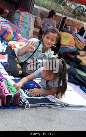 Ein jungen Lao Mädchen gibt die "OK" Zeichen auf ihre Mutter Nachtmarkt stall in Luang Prabang Stockfoto