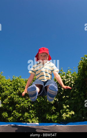 Eine fünf Jahre alte männliche junge Kind Spaß hüpft auf und ab auf eine Trampolene in einem uk-Garten im Sommer Stockfoto