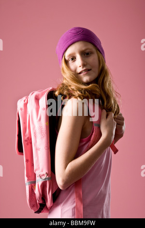 Rothaarige Mädchen tragen eine violette Motorhaube und eine Schultasche vor einem rosa Hintergrund Stockfoto