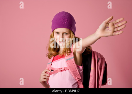 Rothaarige Mädchen tragen eine violette Motorhaube und eine Schultasche vor einem rosa Hintergrund Stockfoto