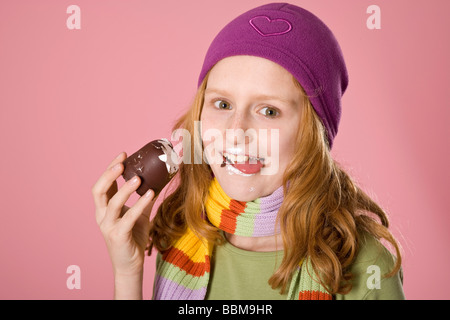 Rothaarige Mädchen tragen eine violette Motorhaube vor einem rosa Hintergrund, Biss in ein chocolate marshmallow Stockfoto