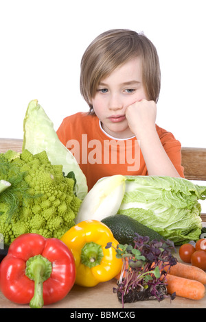 Junge sitzt an einem Tisch voller Gemüse, suchen unglücklich Stockfoto