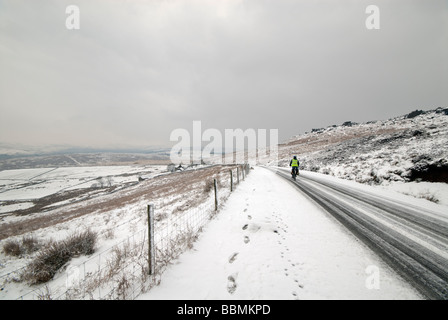 Einsame männliche Radfahrer auf einer entfernten eisigen Schnee bedeckt Straße Stockfoto