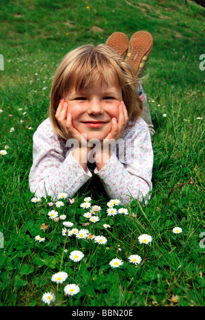 Mädchen, 5 Jahre, liegend auf einer Wiese mit Gänseblümchen (Bellis Perennis) Stockfoto