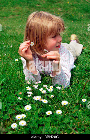 Mädchen, 5 Jahre, liegend auf einer Wiese mit Gänseblümchen (Bellis Perennis) und Blumen in ihren Händen hält Stockfoto