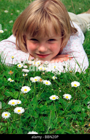 Mädchen, 5 Jahre, liegend auf einer Wiese mit Gänseblümchen (Bellis Perennis) Stockfoto