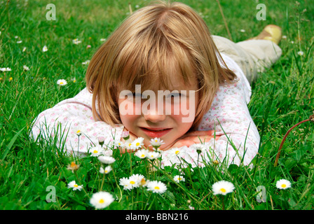 Mädchen, 5 Jahre, liegend auf einer Wiese mit Gänseblümchen (Bellis Perennis) Stockfoto