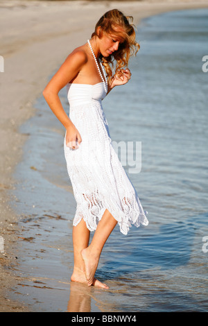 Junge blonde weiße Frau in einem weißen Sommerkleid, ihre Zehen in das Wasser am Strand. Stockfoto