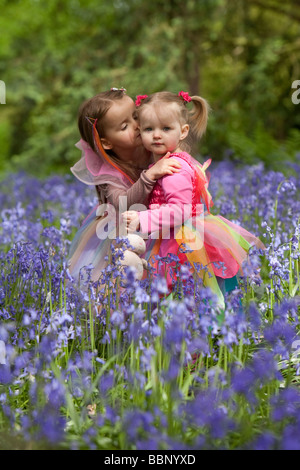 Zwei Kleinkinder in Fee Kleider küssen in einem Holz voller Glockenblumen in England. Stockfoto