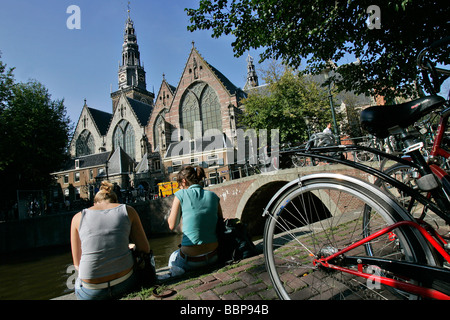 ENTSPANNEN AM UFER EINES KANALS VOR DER "OUDE KERK" KIRCHE, ROTLICHTVIERTEL, AMSTERDAM, NIEDERLANDE Stockfoto