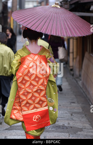 Ein Lehrling Geisha oder Maiko, zu Fuß entlang einer Gasse in der Gion Bezirk von Kyoto mit einem Regenschirm Stockfoto