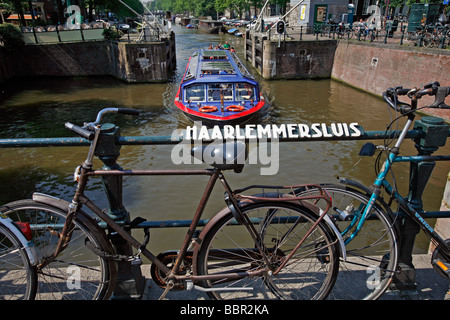 HOLLANDRÄDER AN DAS GELÄNDER DER HAARLEMMERSLUIS-BRÜCKE AUF DIE SINGEL GRACHT UND SIGHTSEEING-BOOT VERLASSEN EINE SPERRE ANGEBRACHT Stockfoto