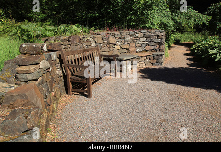 Eine Holzbank, eingebettet in eine geschwungene Trockenmauer im Garten eines Anwesens auf der Isle Of Skye. Stockfoto