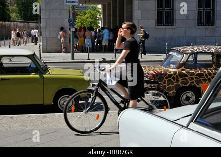 FRAU AUF EINEM FAHRRAD UND EINEN TRABANT, DAS FAMILIENAUTO DER EX-DDR WERDEN EIN KULTAUTO, BERLIN, DEUTSCHLAND Stockfoto