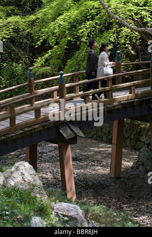 Ein paar Übergang über eine sanft gewölbte Holzbrücke in einem japanischen Garten am Schlosspark Hamamatsu Stockfoto